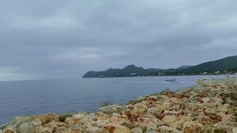 Boats-on-the-sea-of-Cala-Ratjada-in-Mallorca-on-the-coast-with-big-stones-and-mountains-in-the-background