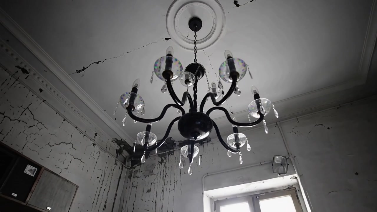 Starting cam on chandelier, panning and tilting in decayed room, showing cracked ceiling, wiring