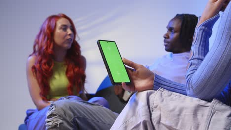 Close-Up-Of-Woman-With-Green-Screen-Mobile-Phone-Sitting-With-Gen-Z-Friends-Talking-And-Sharing-Posts-4