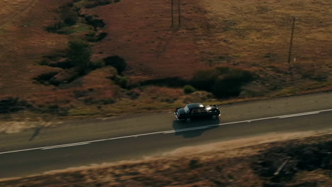 un dron disparó junto a un auto antiguo black austin westminster conduciendo a través de las colinas de sudáfrica durante el invierno seco 4k
