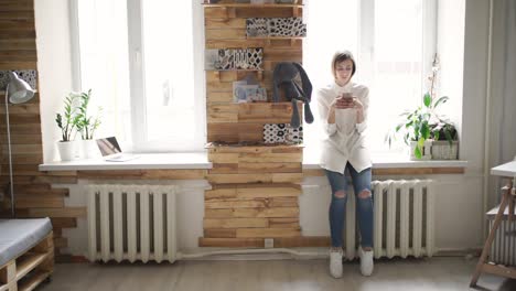 beautiful woman using mobile phone standing front window in room