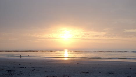 sunrise on a cloudy day at the beach, people taking an early morning swim