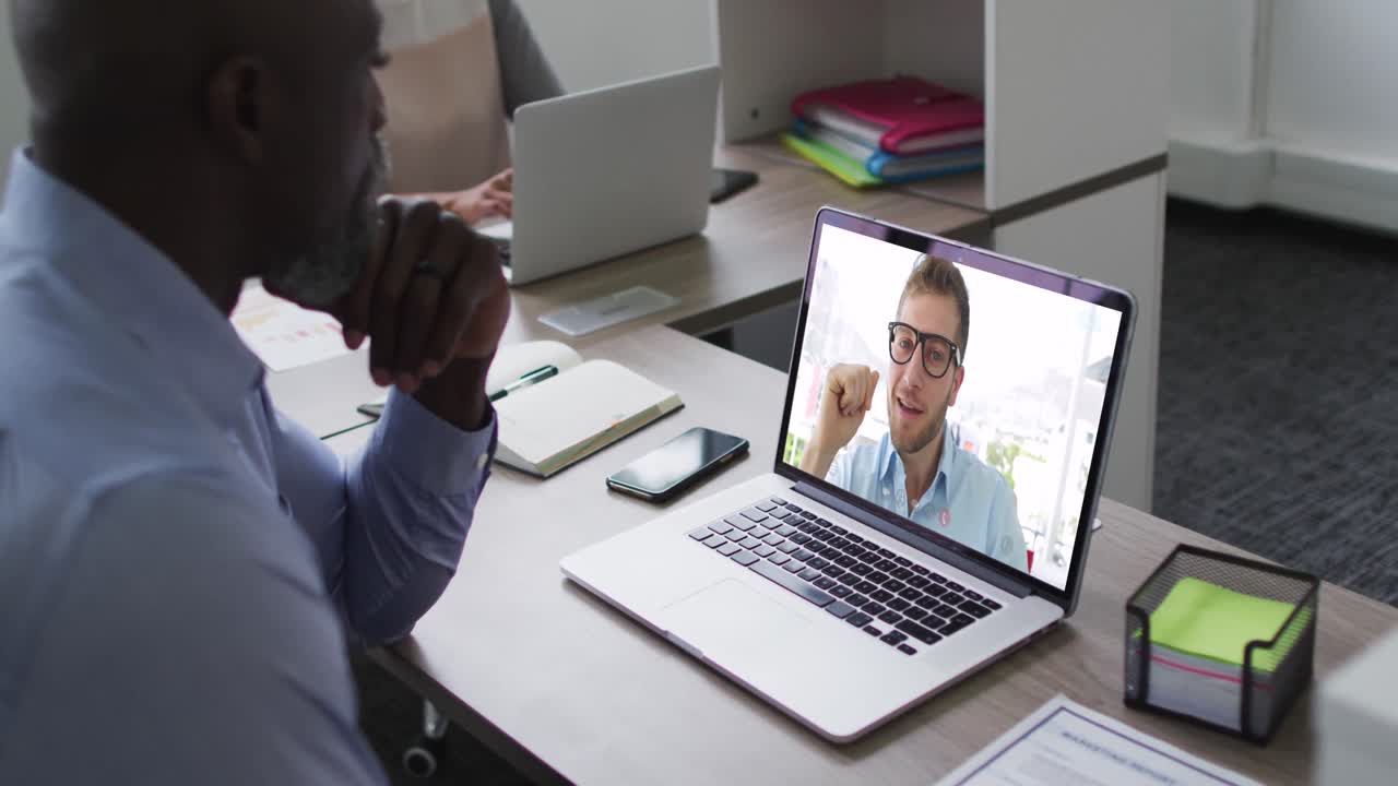 African american senior man having a video call with male colleague on laptop at office