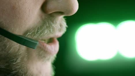 Extreme-closeup:-Bearded-male-talks-on-phone-headset,-bright-lights