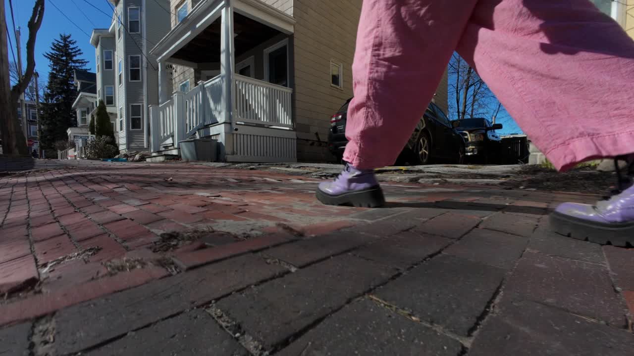 Camera tracks person walking down street, wearing purple shoes and pink pants in Portland, Maine, USA.