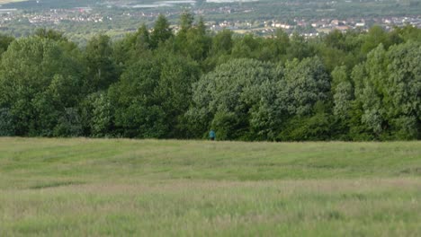 Hand-held-tracking-shot-of-a-female-walking-her-dog-in-a-field-and-raising-her-arms