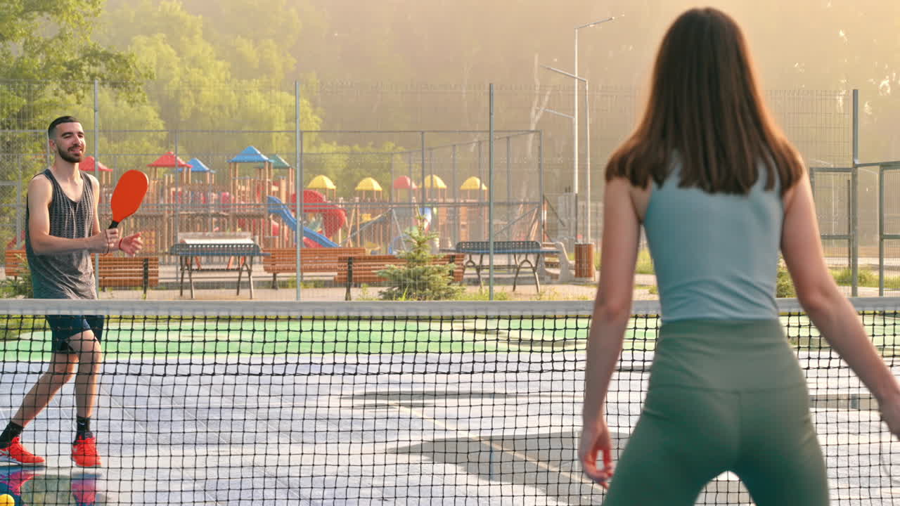 A man and a woman playing pickleball at sunrise, after rain
