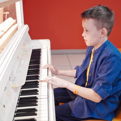 side view of a child playing the white piano. young boy learns how to play the piano. piano lessons. kid and musical instrument. musical education. hobbies.