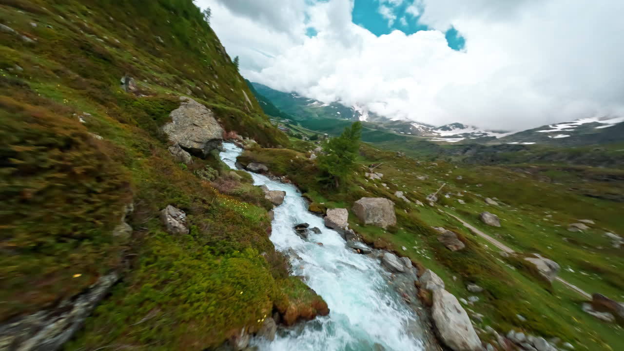 A scenic aerial view of a winding mountain stream flowing through lush green meadows near Cervinia