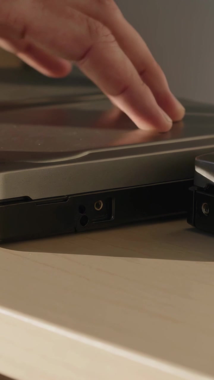 Vertikal video: Rækkende hånd skubber metal-clamshell-enhed på lyst skrivebord og inspicerer sideporte.