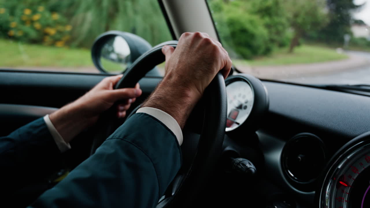 Close up of a man's hands on a steering wheel, driving a car on the road