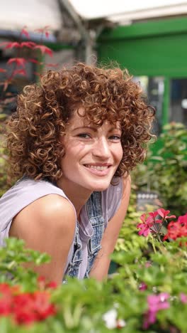 woman gardener smiling and looking at flowers in greenhouse. vertical