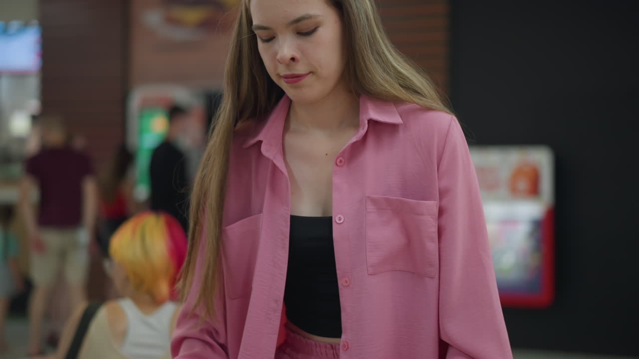 햄버거, 김, 음료를 가진 트레이를 들고 있는 백인 여성이 그녀의 테이블을 향해 걸어가고, 쇼핑 가방이 의자 위에 놓여 있고, 그녀의 가방은 테이블 위에 있고, 색의 머리카락을 가진 여성이 그녀의 뒤에 앉아 있습니다.