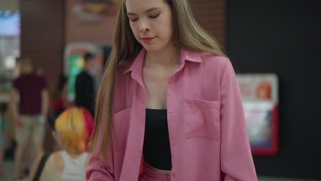 dama blanca llevando una bandeja con hamburguesa, papas fritas y bebida camina hacia su mesa, la bolsa de compras se coloca en la silla mientras su bolsa está en la mesa, una mujer con cabello de color se sienta detrás de ella