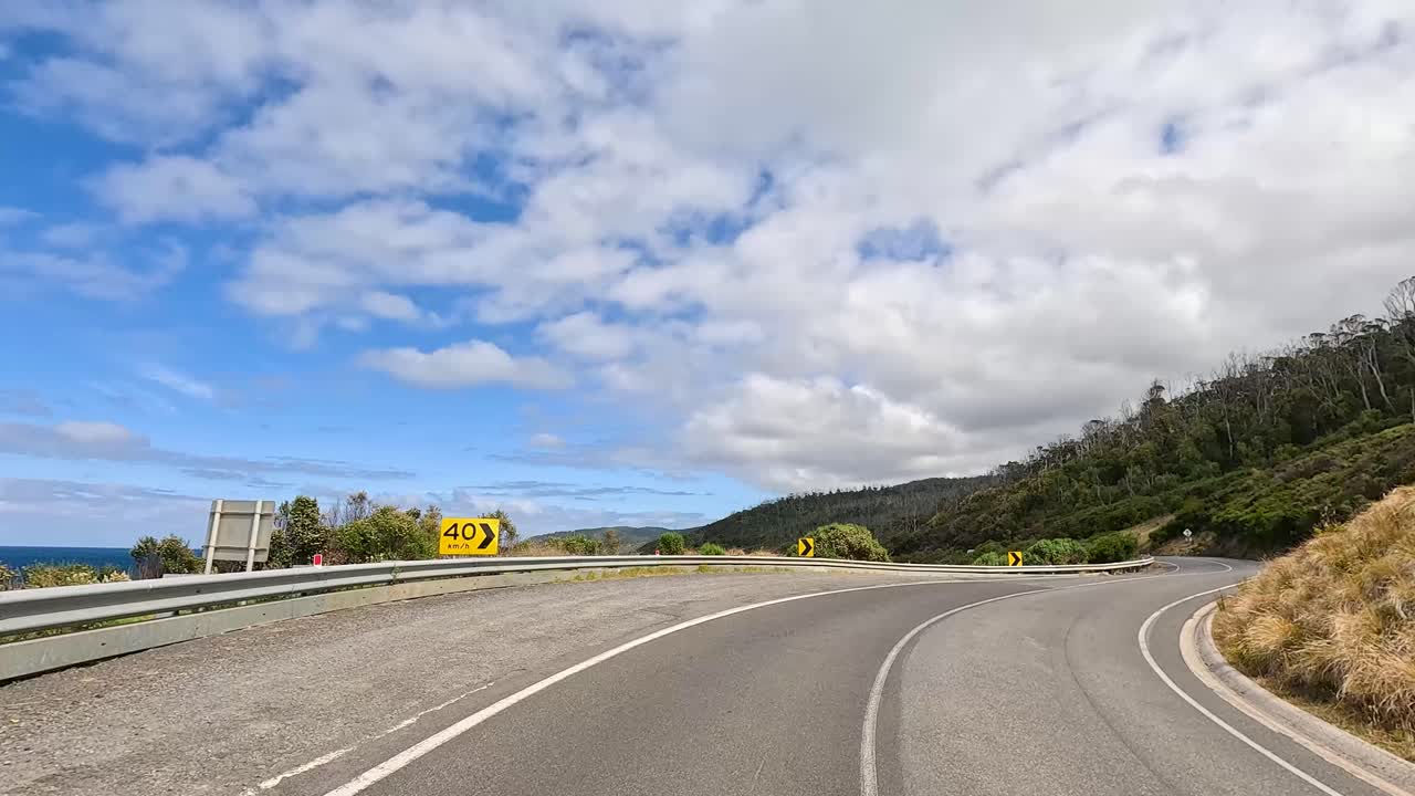 A 12-second drive along the Great Ocean Road, showcasing lush greenery, ocean views, and winding roads under a partly cloudy sky