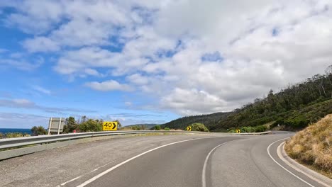 a 12-second drive along the great ocean road, showcasing lush greenery, ocean views, and winding roads under a partly cloudy sky