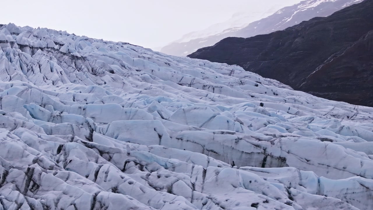 Vidstrakt isbrefelt med ulendte sprekker under mørke fjellsider