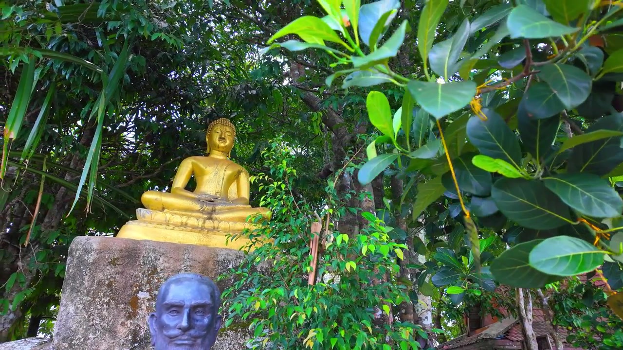 Una piccola statua dorata di Buddha immersa tra alberi verdeggianti vicino al Grande Buddha di Phuket, Thailandia.