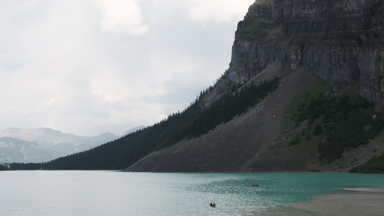 Two canoes glide across serene turquoise waters with a towering mountain in the background
