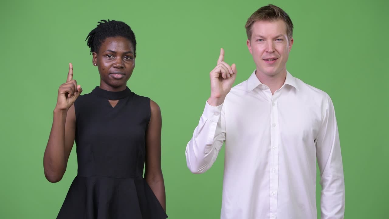 Two young multi-ethnic business couple pointing up together