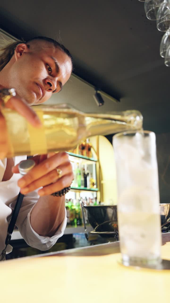 Barman che versa un drink in un bicchiere con ghiaccio in un bar.