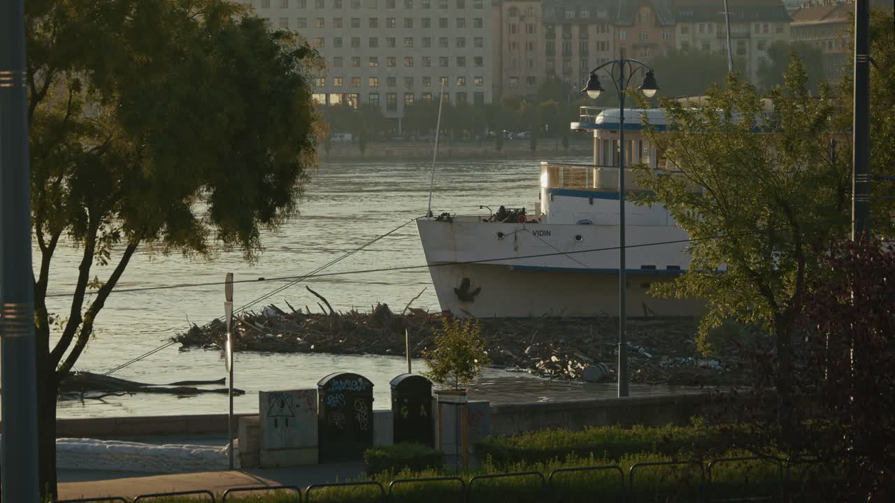 Boat surrounded by debris along the river with a passing tram in the foreground, Budapest, Hungary