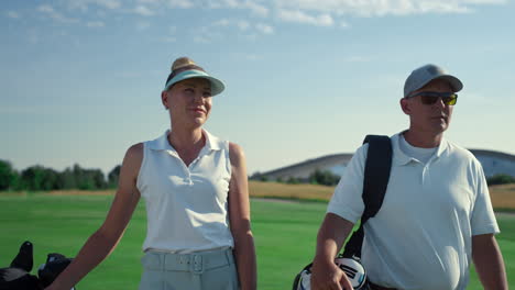 golf players couple walk together on lush course. rich people chatting in summer