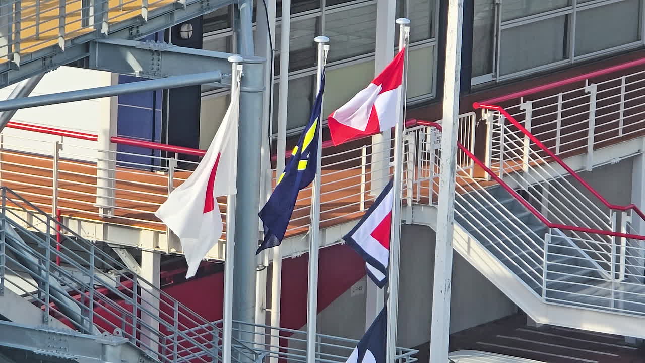 Assorted international and maritime signal flags flying on poles by stairs and railings, vibrant colors against urban Osaka architecture, evoking port activity, travel and trade