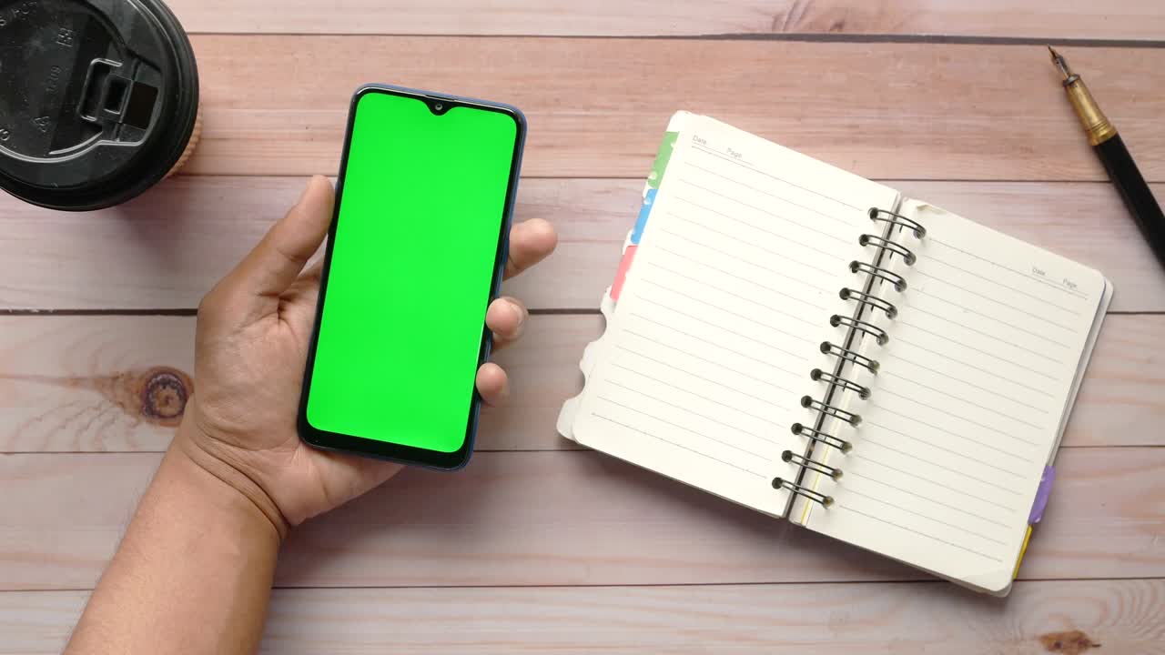 young man hand holding smart phone with green screen on table