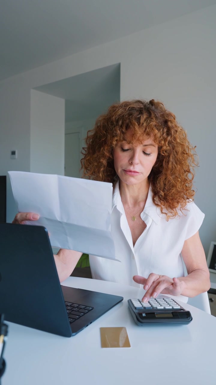 Donna che calcola le spese mentre esamina documenti cartacei nell'ufficio di casa.