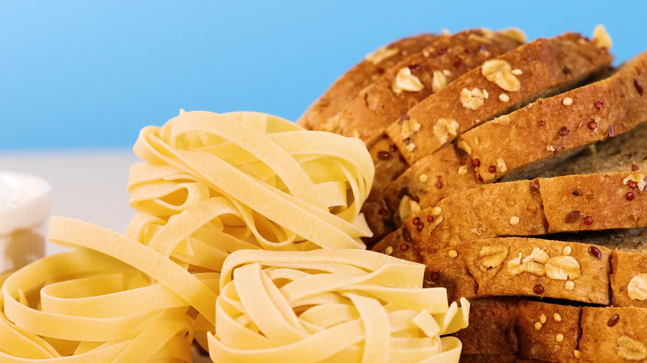 Et utvalg av korn, pasta og brød vises på en blå bakgrunn, som fremhever tekstur og fargekontrast.