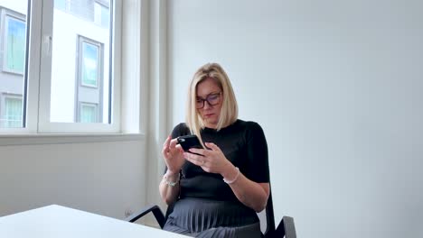 Hermosa-Mujer-Rubia-Sentada-En-La-Sala-De-Reuniones-Enviando-Mensajes-De-Texto-Por-Teléfono