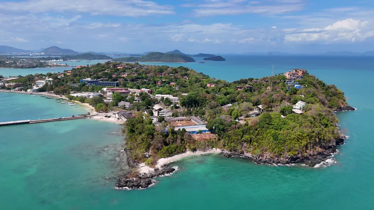 Drone footage captures Cape Panwa's lush greenery and turquoise waters under clear skies, showcasing the scenic beauty of Phuket, Thailand
