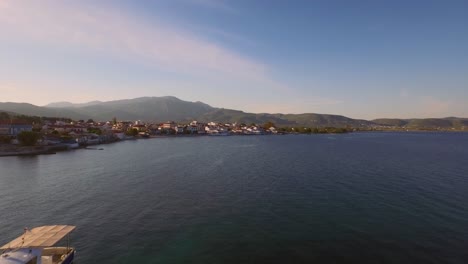 Aerial:-Small-fishing-town-with-Greek-flag-on-Samos-island,-Greece