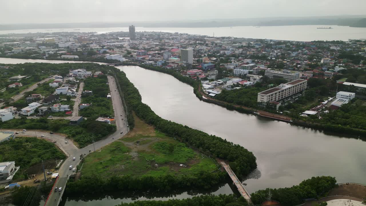 Sorvolo aereo dell'Iloilo River Esplanade con il fiume sinuoso, lo sviluppo urbano e il paesaggio cittadino circostante a Iloilo City, Filippine