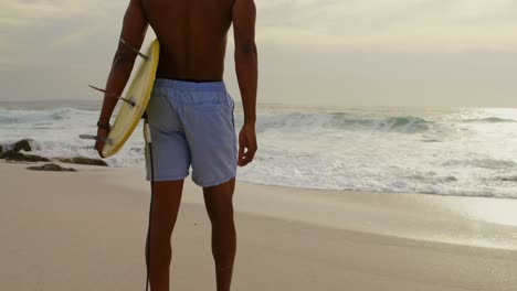 Rückansicht-Eines-Männlichen-Surfers,-Der-Mit-Einem-Surfbrett-Am-Strand-Läuft,-4k
