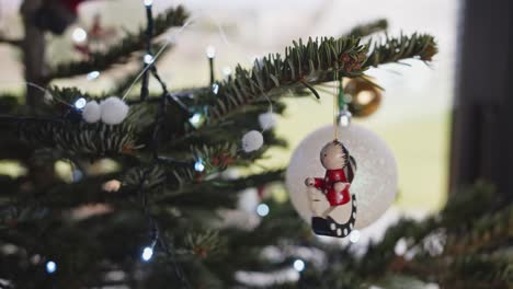 colgando una pequeña decoración de madera colorida en el árbol de navidad al lado de la ventana moderna 4k