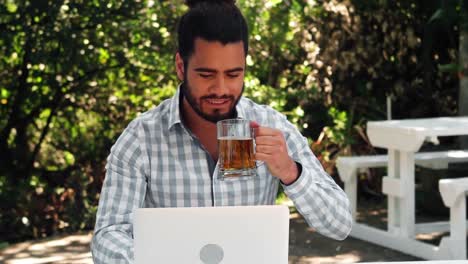 Hombre-Sonriente-Bebiendo-Un-Vaso-De-Cerveza-Mientras-Trabaja-En-La-Computadora-Portátil