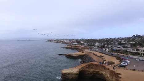 Antena-Siguiente-Pelícanos-Volando-Sobre-Acantilados-Al-Atardecer-En-Pacific-Beach,-San-Diego,-California