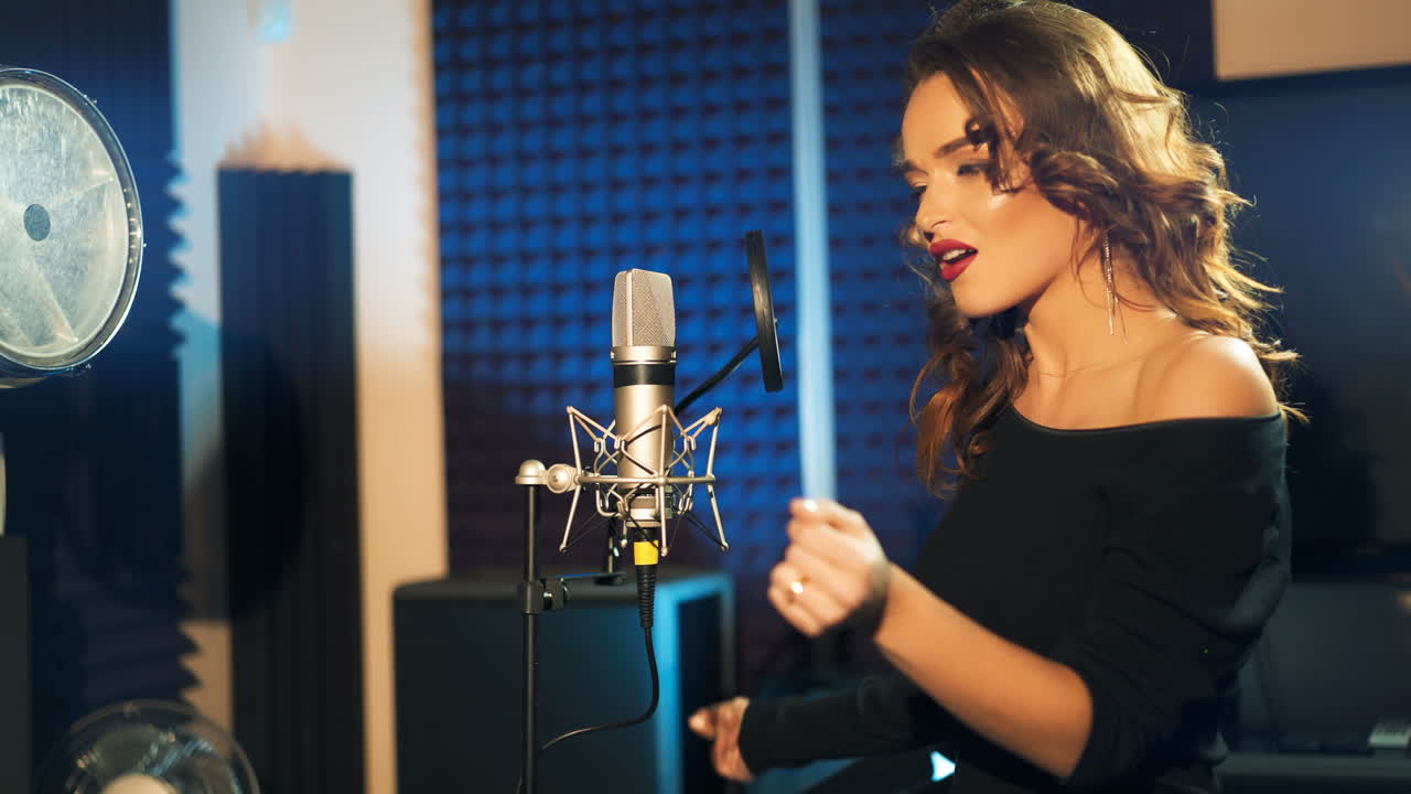 gorgeous woman with long hair is singing and dancing near the microphone in the audio studio on a blue background. Song recording.
