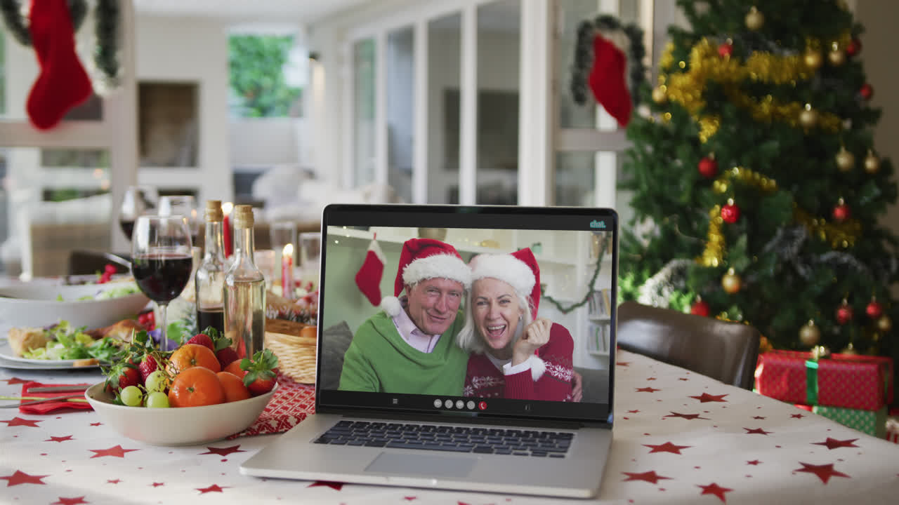 felices abuelos caucásicos con sombreros de papá noel en la computadora portátil en la mesa de navidad
