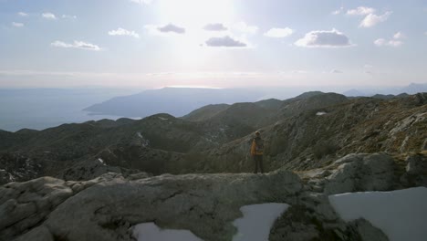 fly over man standing on ridge looking to idyllic mountain and sea view, sveti jure, croatia. aerial forward