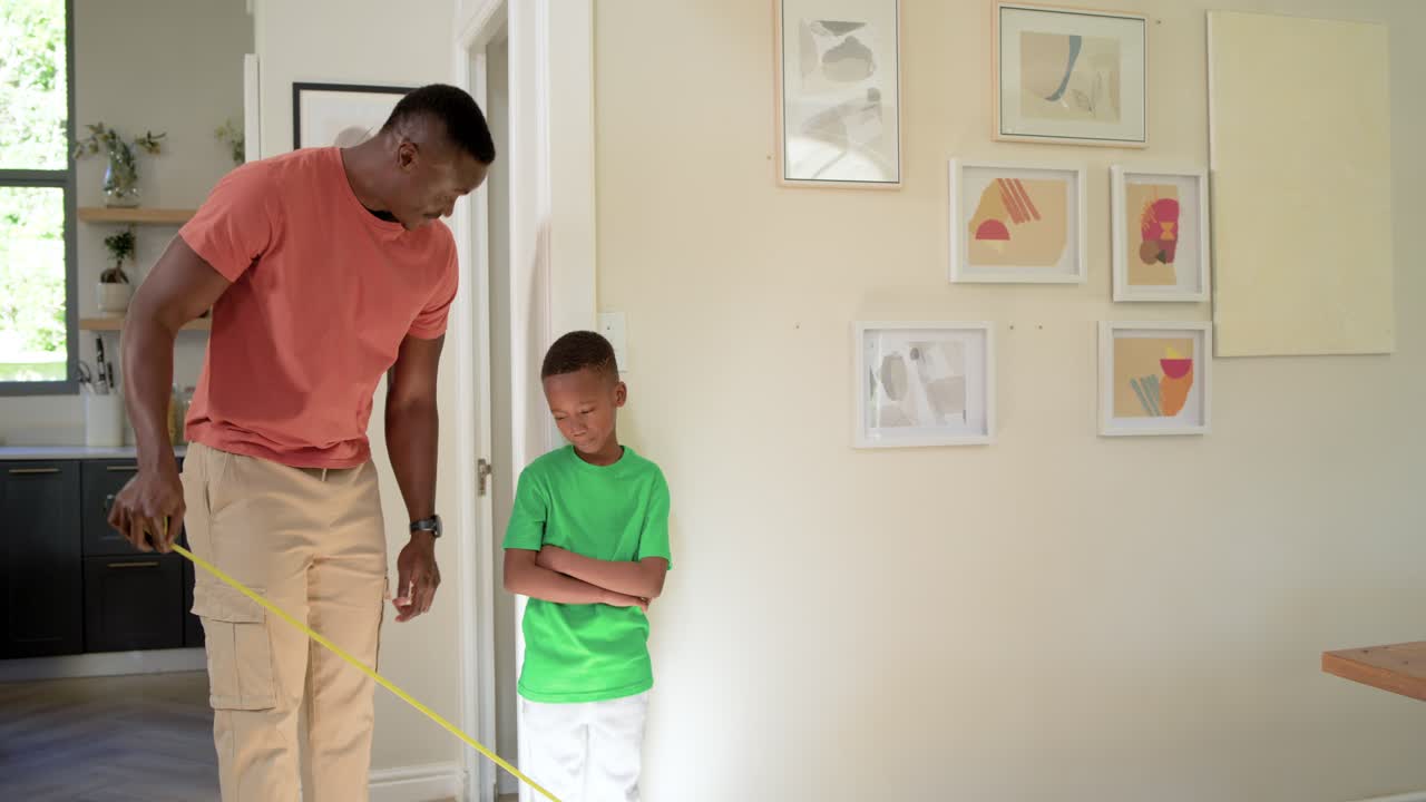 African American father and child bringing yellow tape, aligning and marking hallway wall height