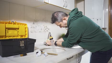 el hombre tratando de arreglar el grifo roto. el agua está brotando del grifo.
