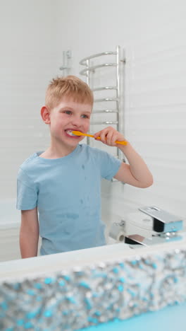 boy brushing teeth in bathroom standing in front of mirror doing morning cleaning with toothbrush