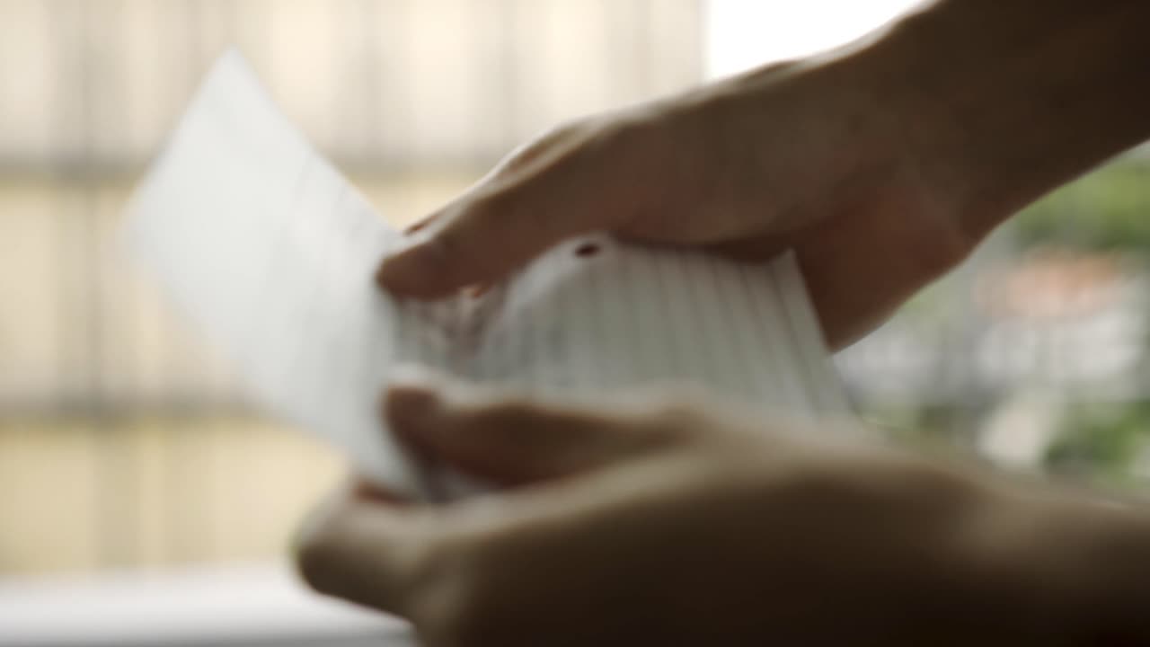 Close up of a person opening a piece of paper and handing it to another person while closing it