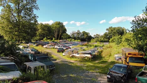 low aerial pan left of junkyard full of wrecked cars and school bus on sunny summer afternoon