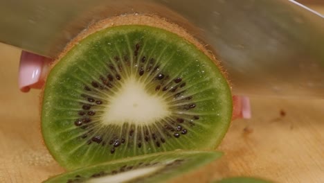 close-up of a woman cutting a ripe fresh kiwi with a knife on a wooden board.