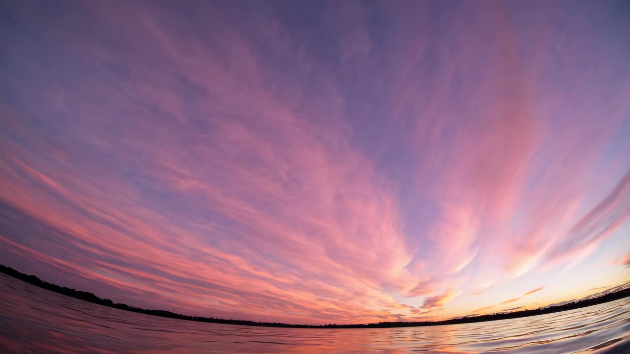 Wide-angle video captures a serene sunset over a calm lake, with vibrant pink and purple clouds
