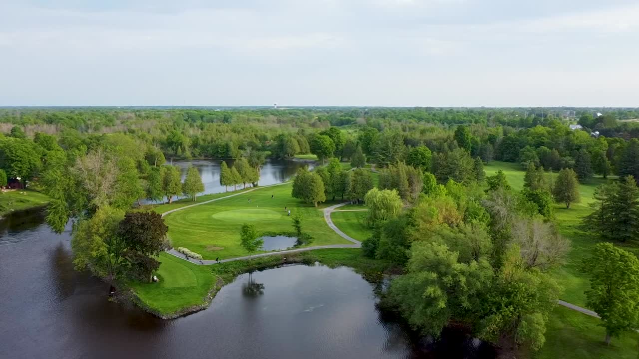 дрон кружит над полем для гольфа, окруженным озером.